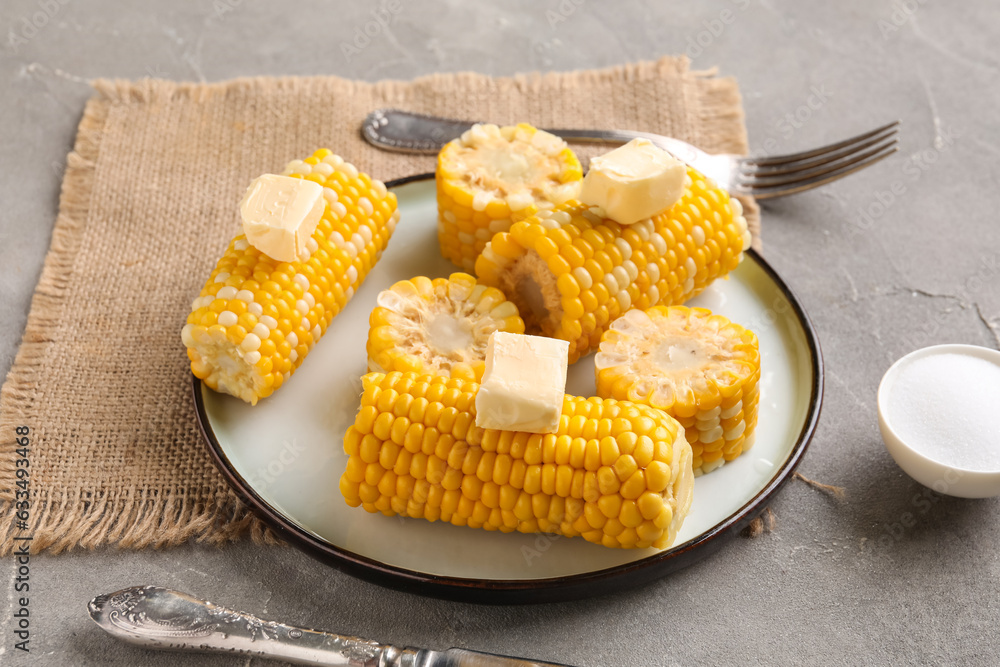 Plate of boiled corn cobs with butter on grey background