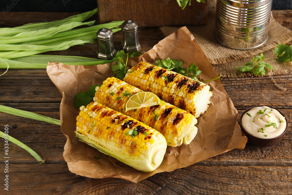 Baking paper with tasty grilled corn cobs and parsley on wooden table