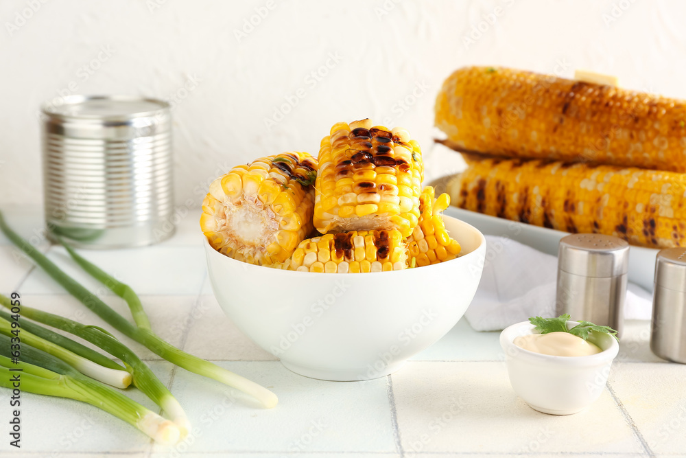 Bowl with tasty grilled corn cobs and green onion on white tile table