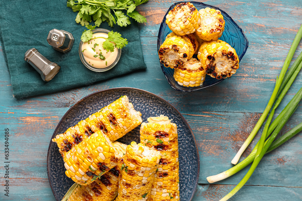 Plate and bowl of tasty grilled corn cobs with parsley on blue wooden background