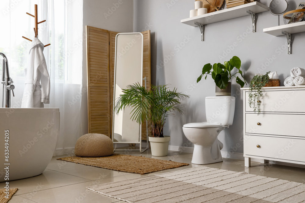 Interior of light restroom with ceramic toilet bowl and houseplants