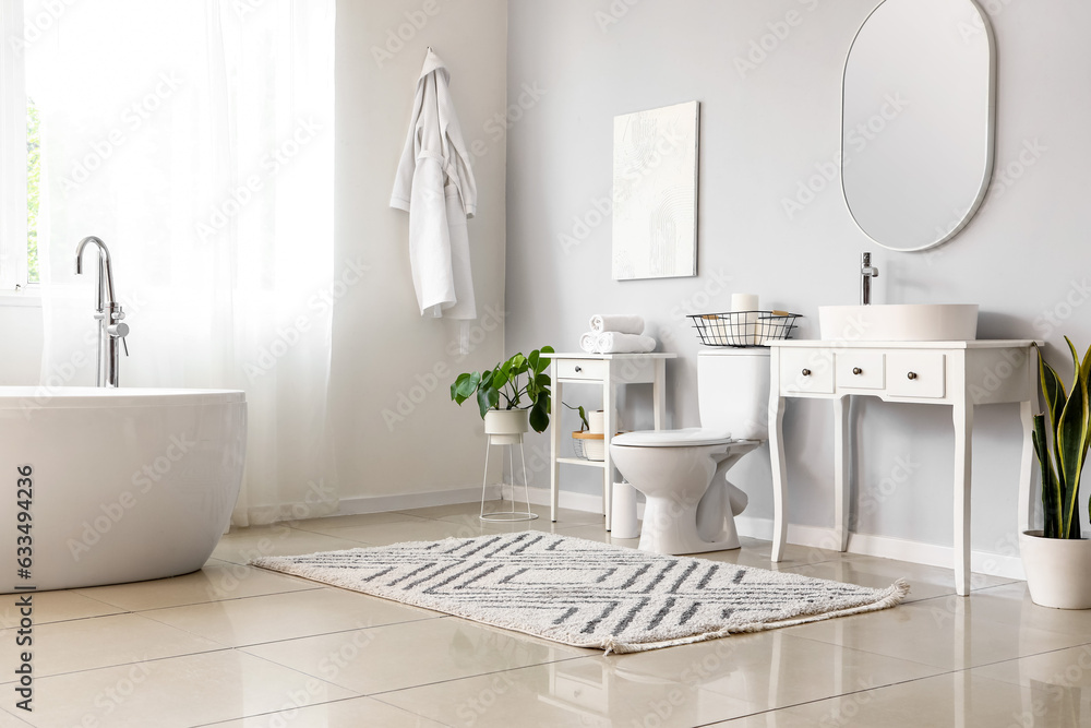 Interior of light restroom with ceramic toilet bowl, bathtub and vanities