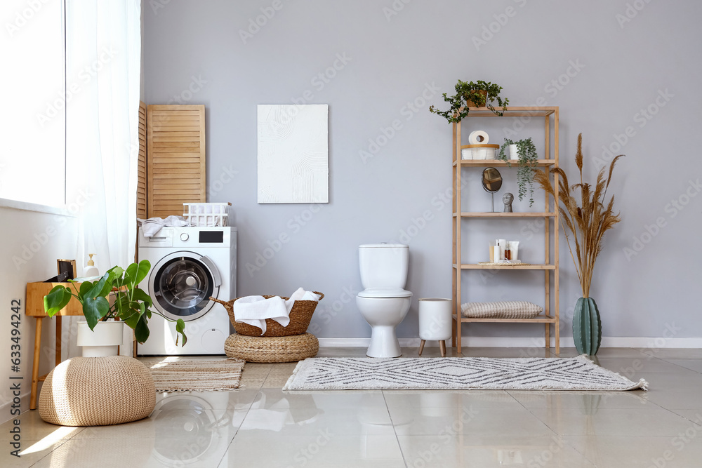 Interior of light restroom with ceramic toilet bowl, shelving unit and washing machine