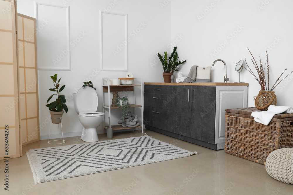 Interior of light restroom with ceramic toilet bowl, vanities and houseplants