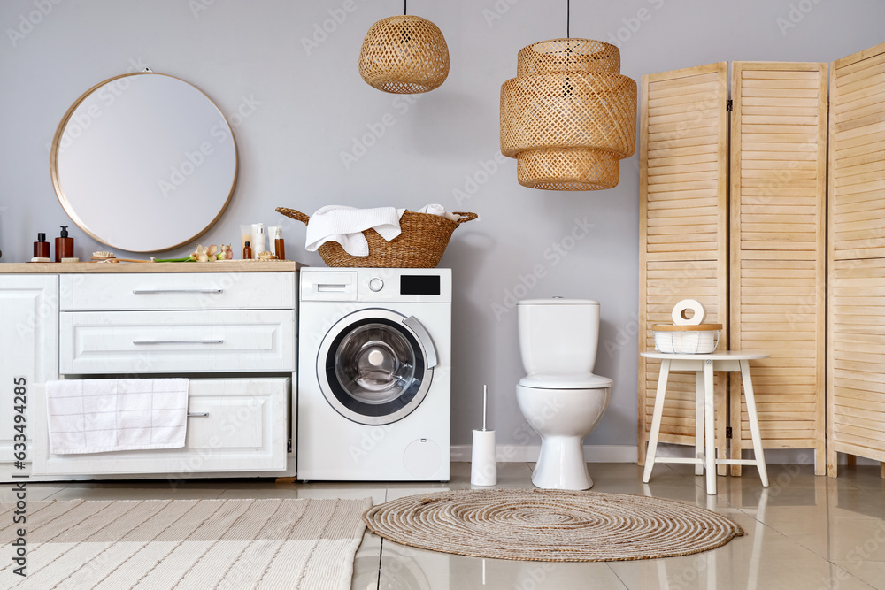 Interior of light restroom with ceramic toilet bowl and washing machine