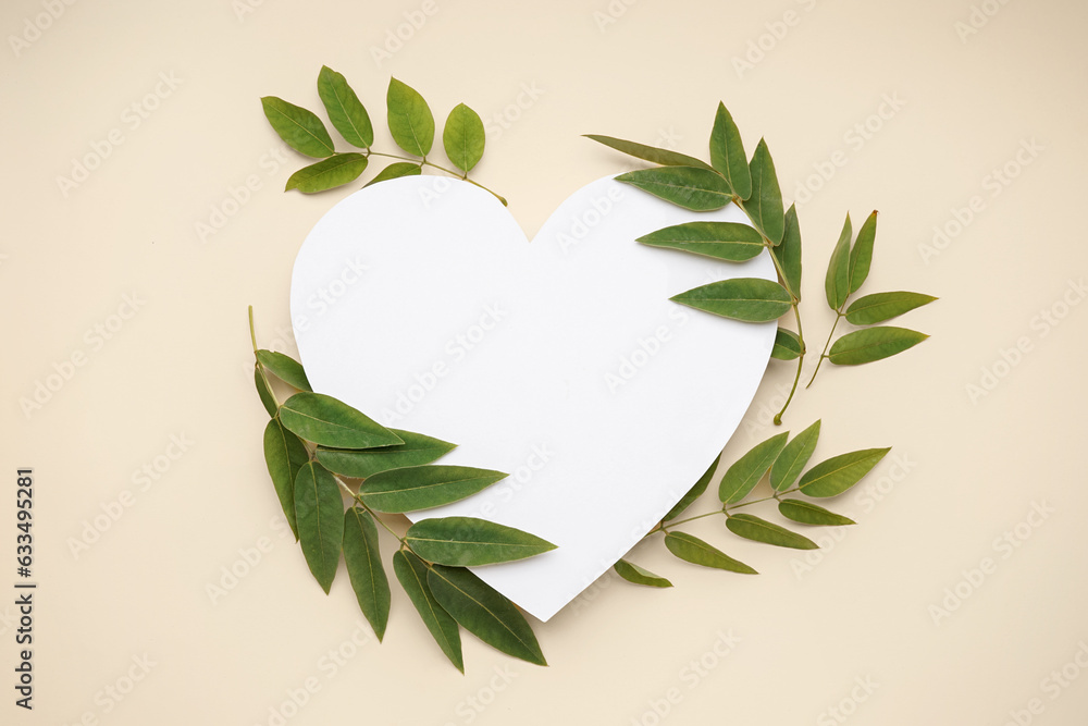 Blank heart shaped card and green plant leaves on color background