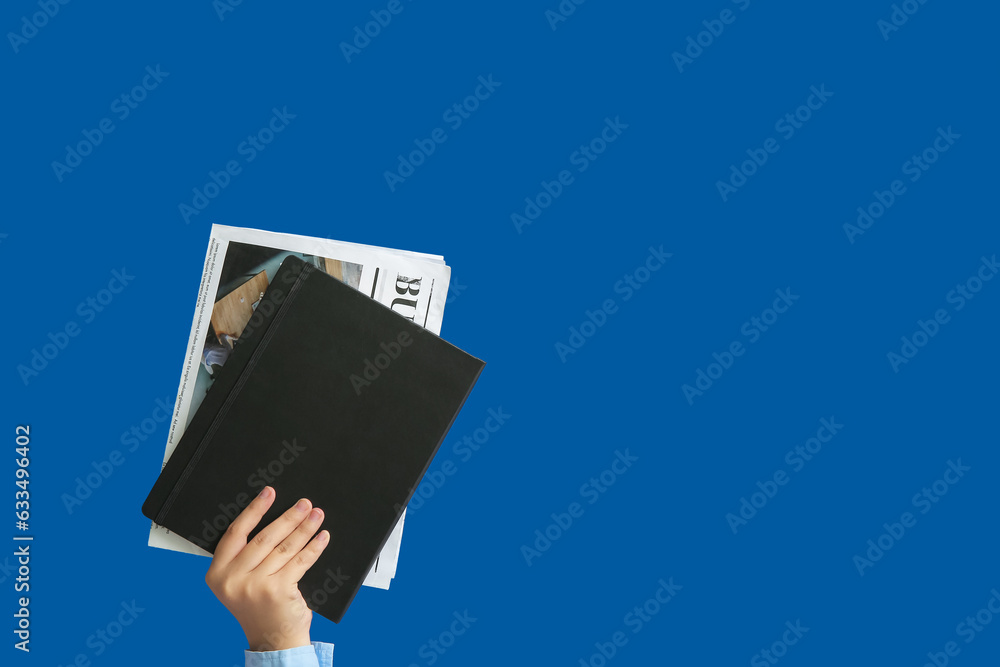 Female hand with notebook and newspaper on blue background