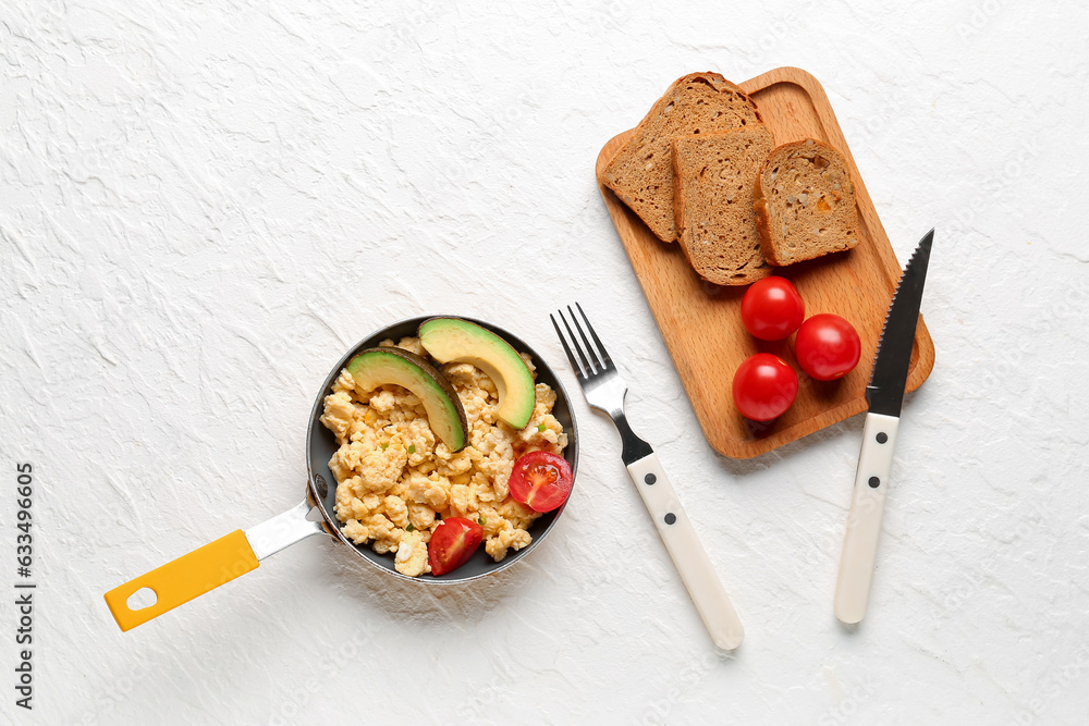 Frying pan of tasty scrambled eggs with avocado and tomatoes on white background