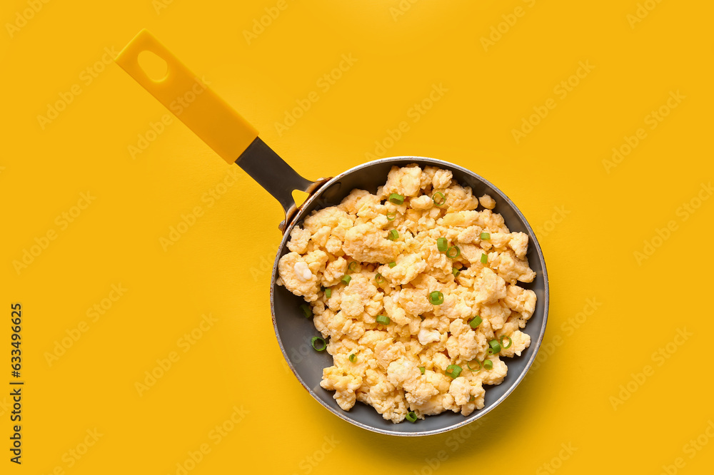 Frying pan of tasty scrambled eggs on yellow background