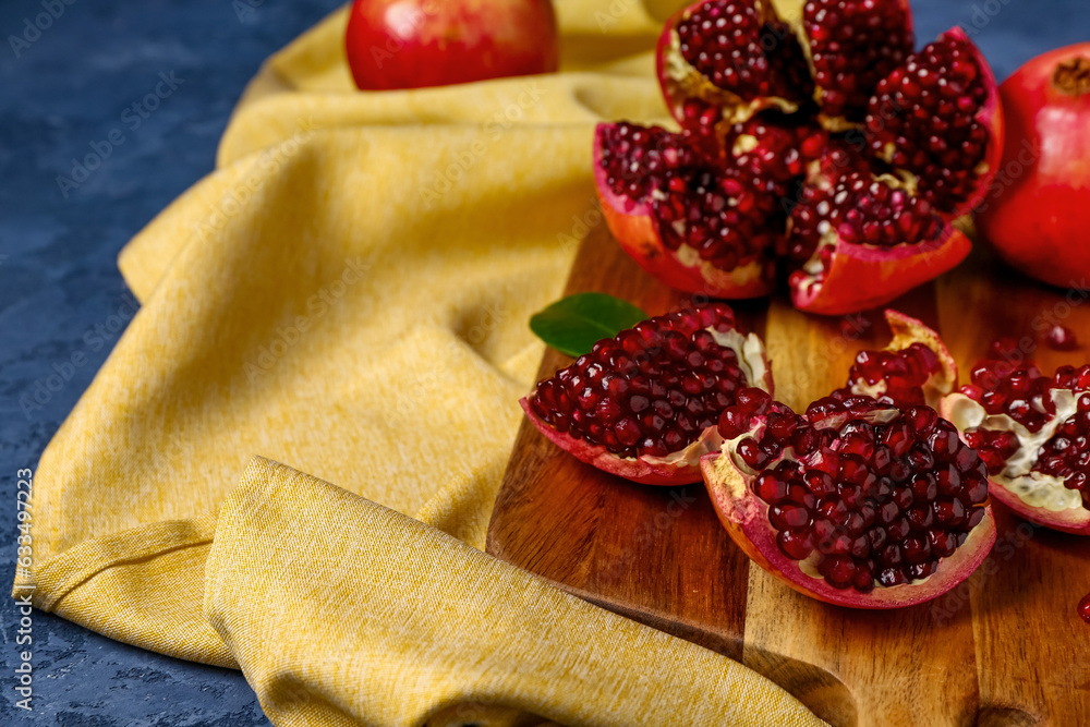 Wooden board with fresh pomegranates on blue background