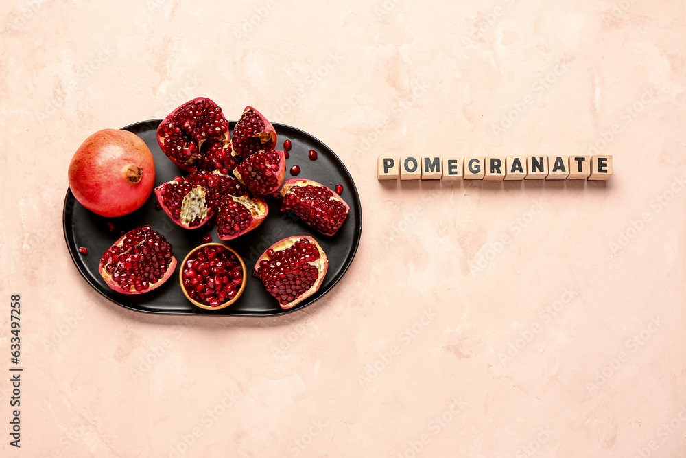 Word POMEGRANATE and plate with fresh fruits on pink background