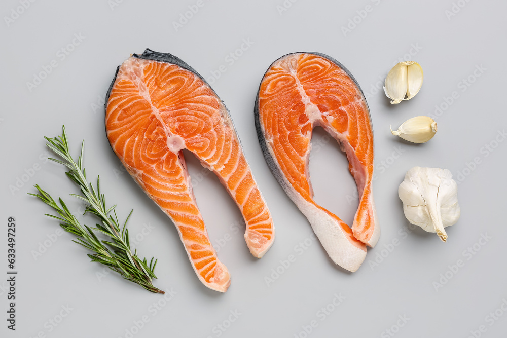 Raw salmon steaks with rosemary and garlic on grey background