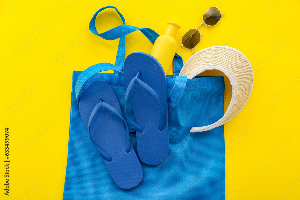 Pair of blue flip flops with cap and sunglasses on yellow background