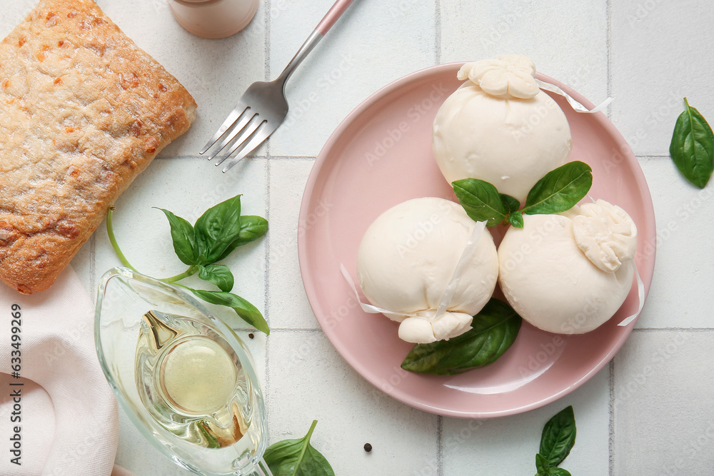 Plate of tasty Burrata cheese with basil and oil on white tile background