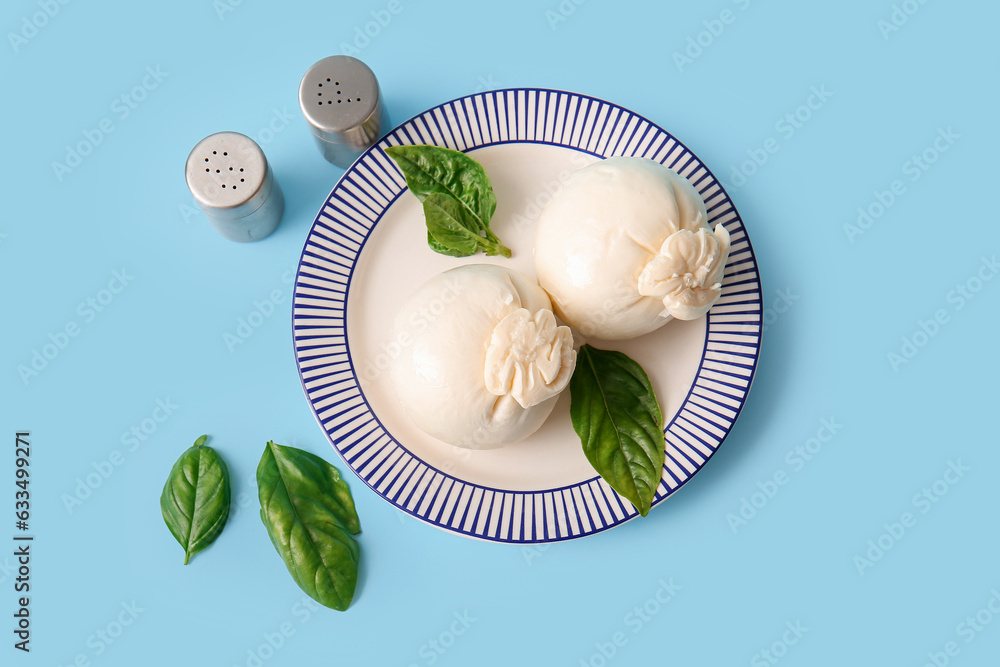 Plate of tasty Burrata cheese with basil on blue background