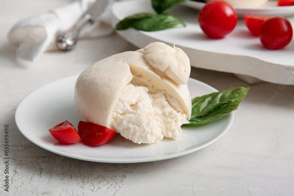 Plate of tasty Burrata cheese with basil and tomatoes on white background