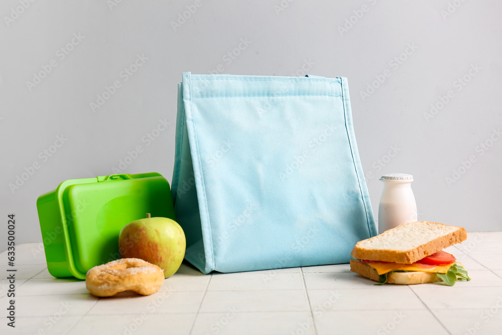 Bag, lunchbox with delicious food and drink on white tile near grey wall