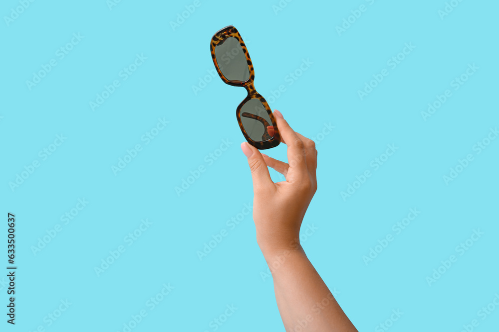 Woman holding stylish sunglasses on blue background