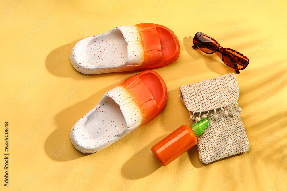 Female stylish flip flops with beach accessories and sunscreen cream on yellow background