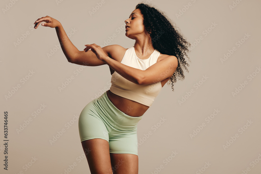 Confident young woman dancing in a studio, wearing fitness clothing