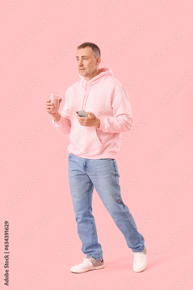 Mature man with glass of fruit smoothie and mobile phone on pink background