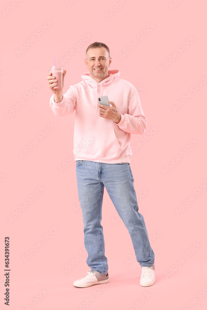 Mature man with glass of fruit smoothie and mobile phone on pink background