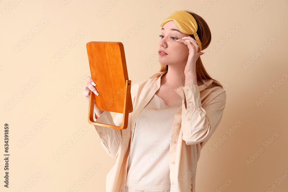 Young woman in pajamas with mirror on beige background