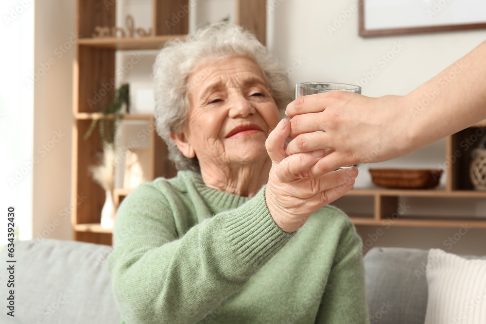 Senior woman taking glass of water from her granddaughter at home, closeup