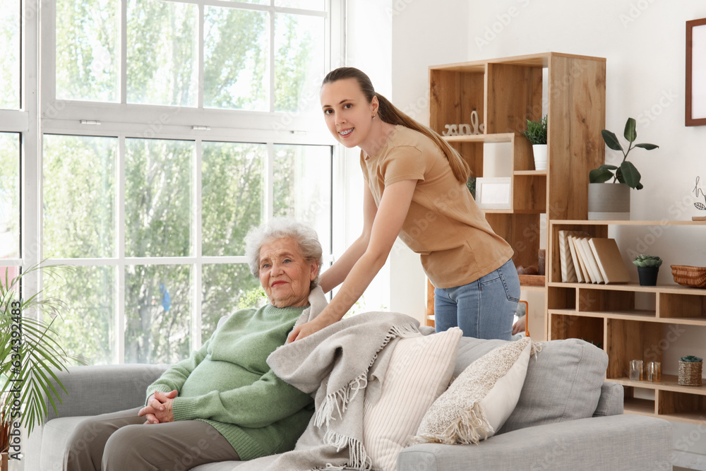 Young woman covering her grandmother with plaid at home