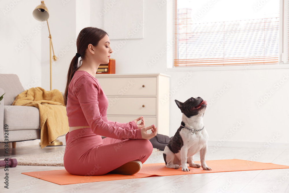 Sporty young woman with her French bulldog meditating at home