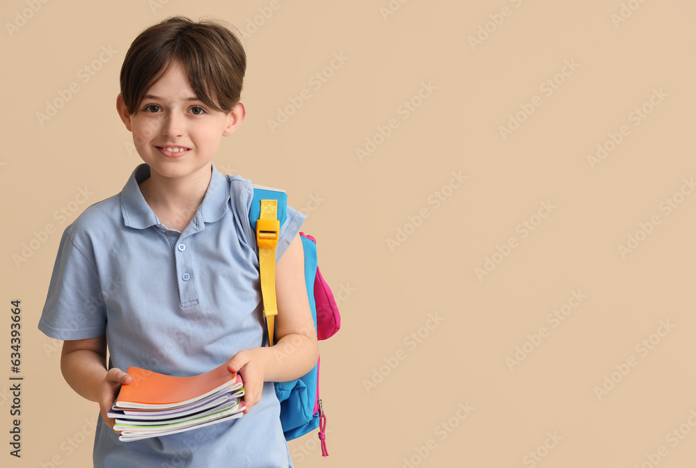 Little schoolboy with copybooks on beige background