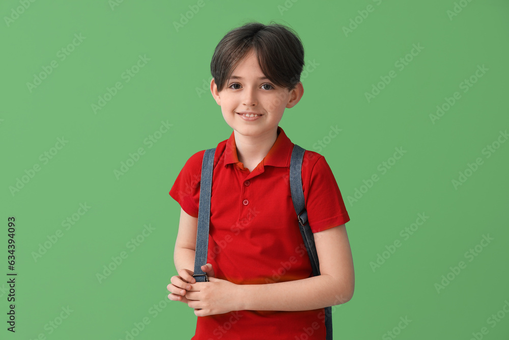 Little schoolboy with backpack on green background