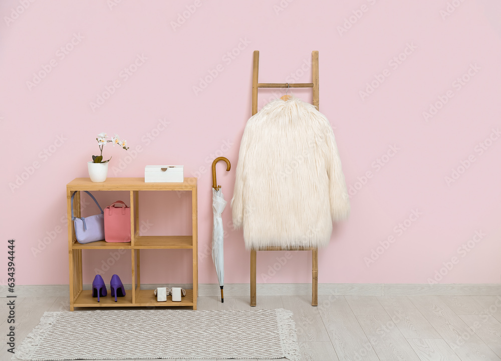 Shelving unit, umbrella and ladder with coat near pink wall in hall