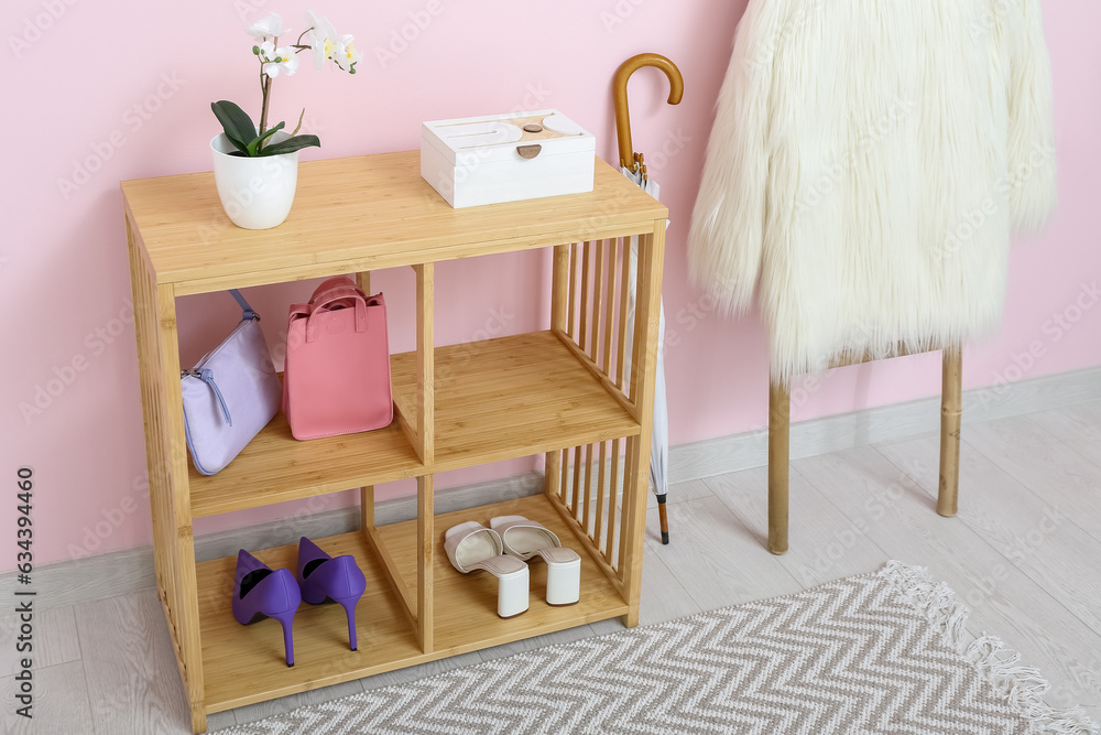 Shelving unit, umbrella and ladder with coat near pink wall in hall