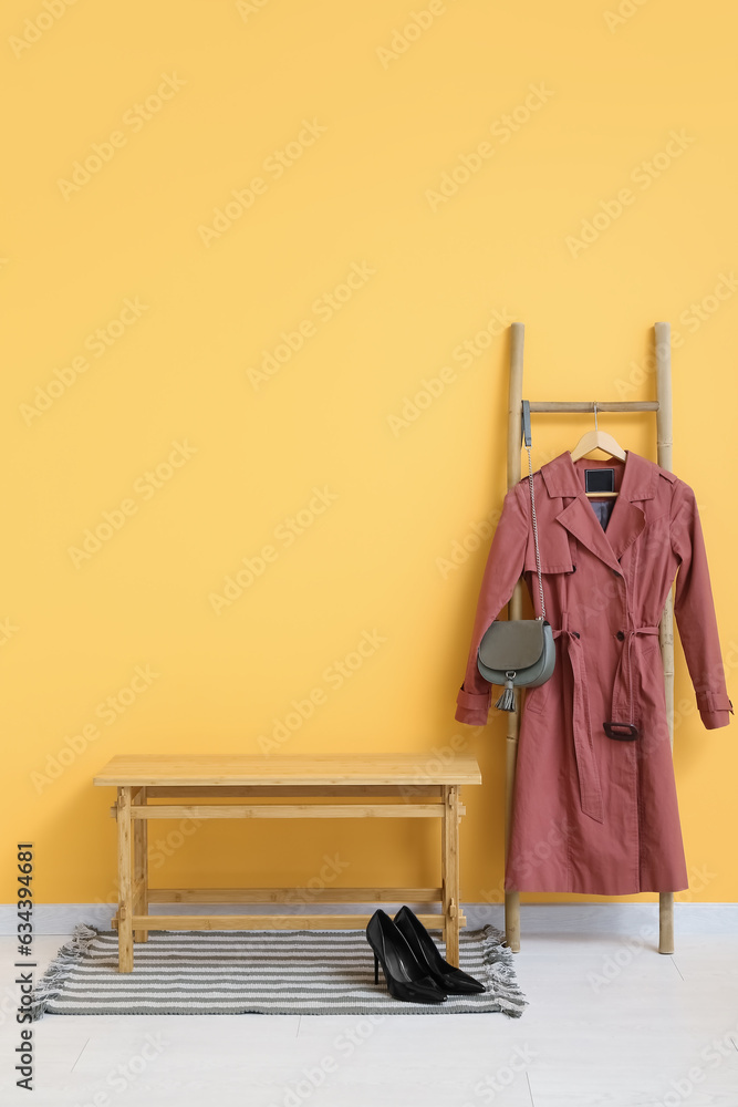 Bench and ladder with coat near orange wall in hall