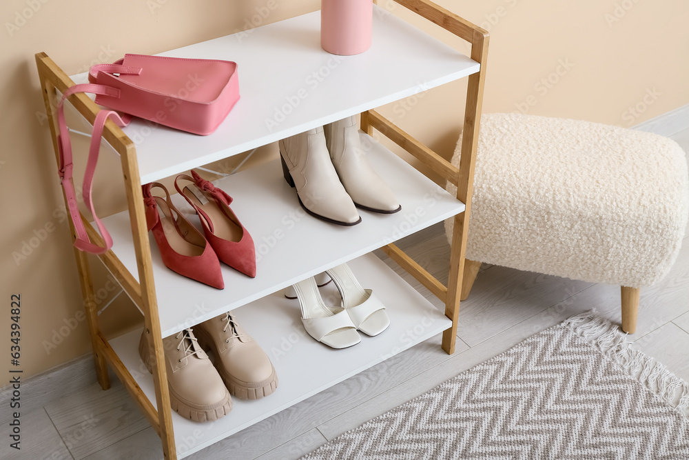 Shelving unit with shoes and bench near beige wall in hall, closeup