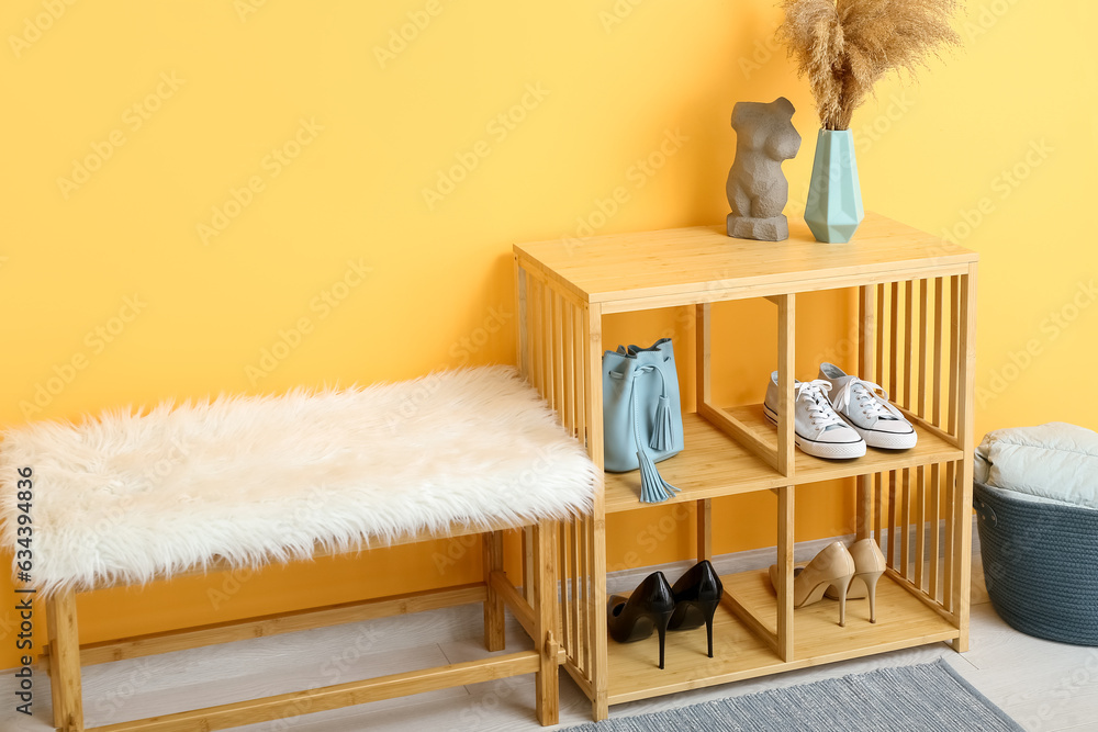 Shelving unit with shoes and bench near orange wall in hall