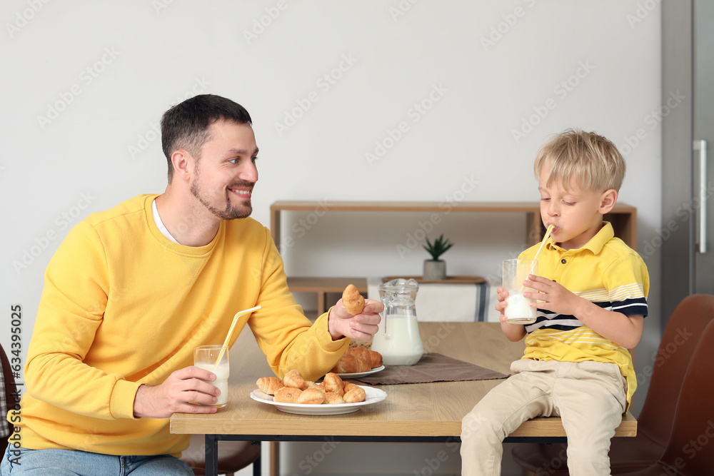 Little boy with his father sitting at table and drinking milk in living room