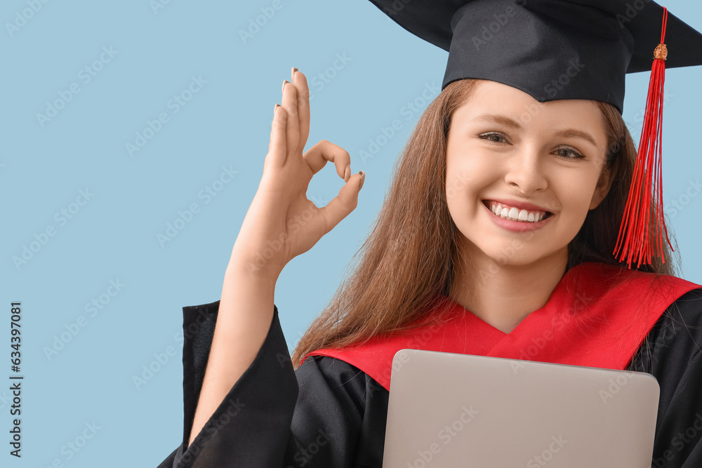 Female graduate student with laptop showing OK on blue background, closeup