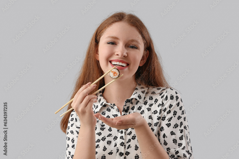 Young woman with tasty sushi roll on grey background