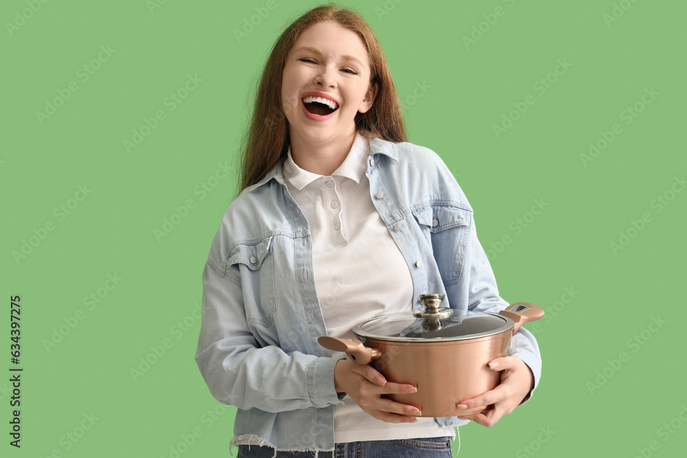 Young woman with cooking pot on green background