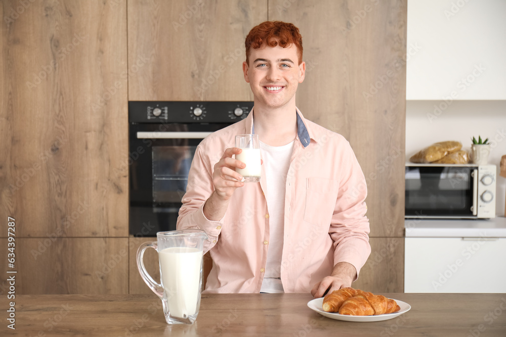 Young redhead man with glass of milk in kitchen