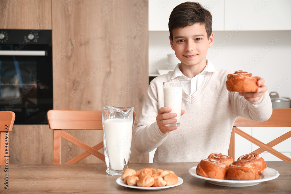 Little boy with glass of milk and tasty bun in kitchen