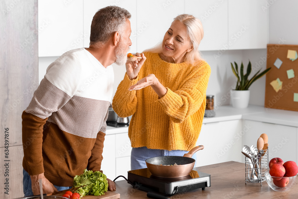 Mature couple tasting food in kitchen