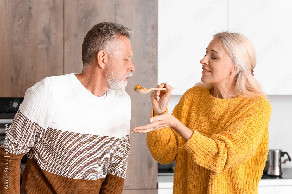 Mature couple tasting food in kitchen