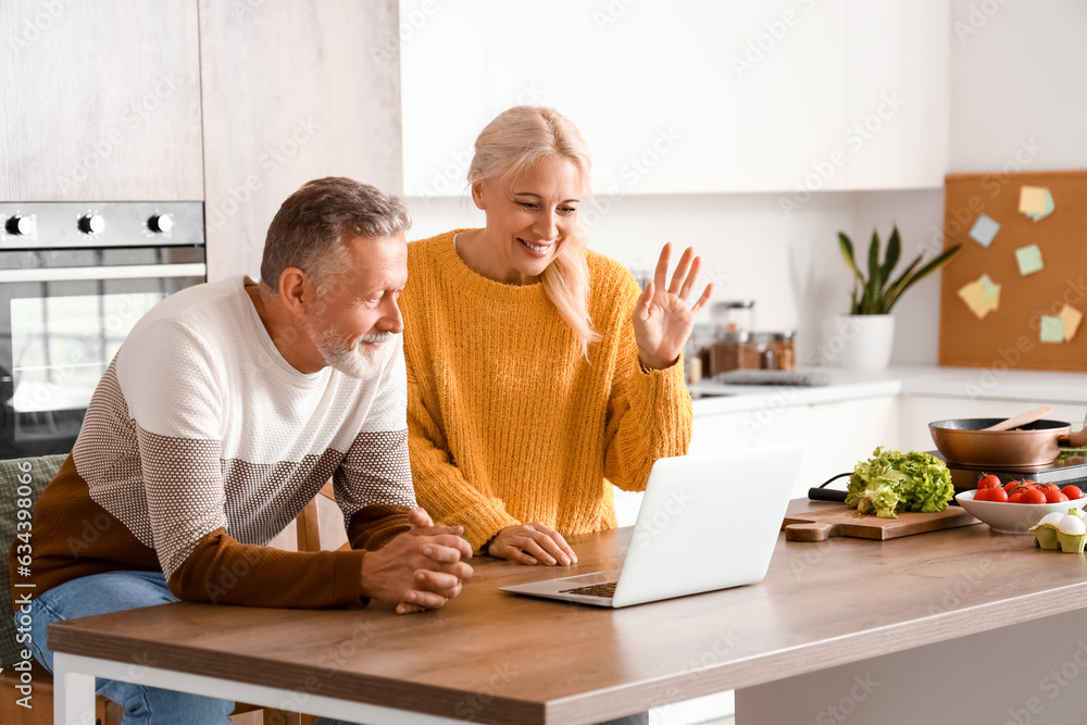 Mature couple with laptop video chatting in kitchen