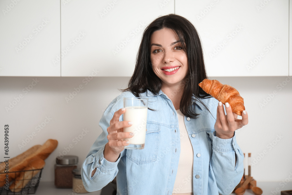 Beautiful woman with glass of milk and tasty croissant in kitchen