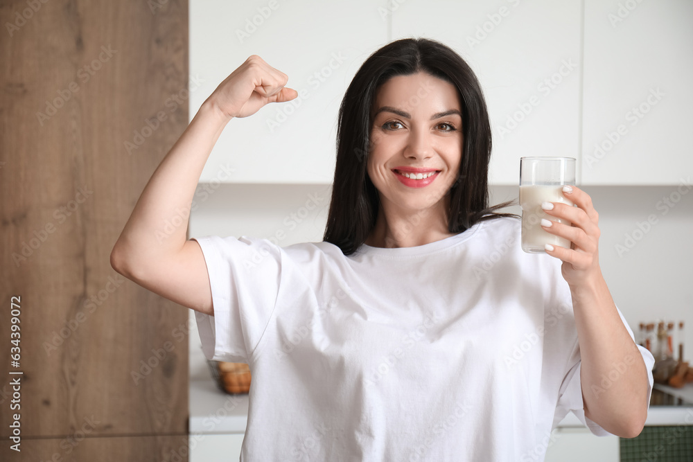 Beautiful woman with glass of milk showing muscles in kitchen