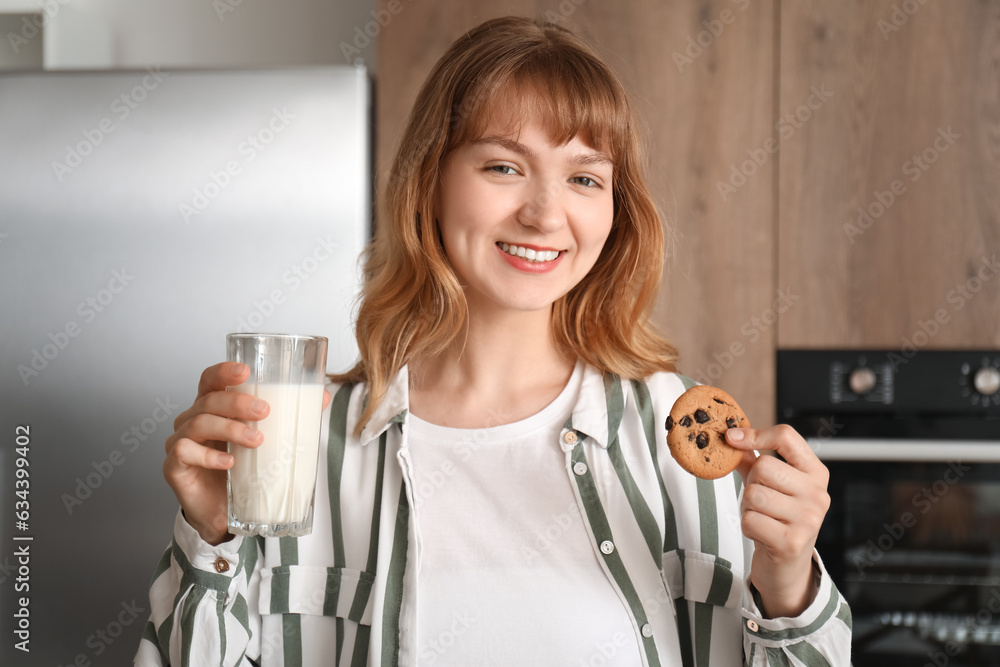 Young woman with cookie and glass of milk in kitchen