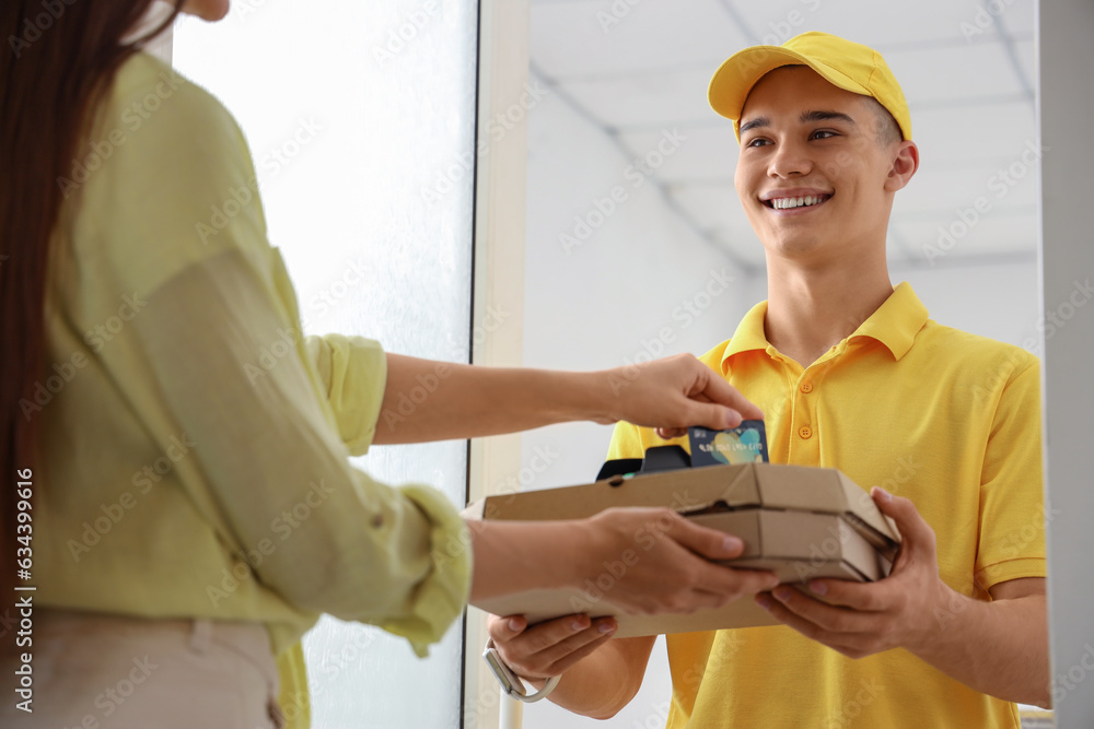 Young courier receiving payment for pizza from woman at doorway